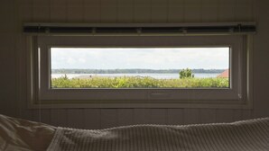 Un dormitorio con un ventanal grande, una cama y vistas a un lago y árboles.