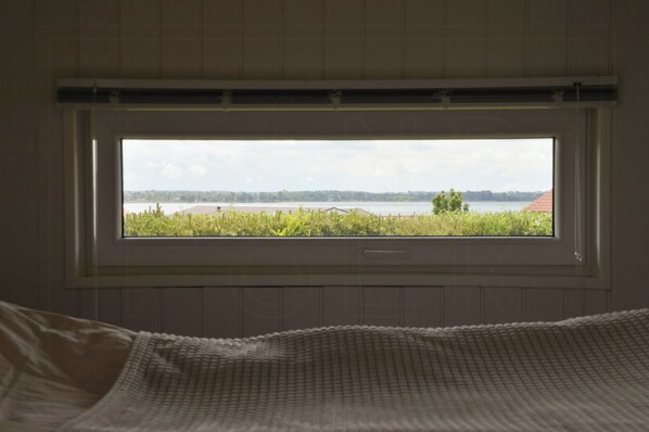 Un dormitorio con un ventanal grande, una cama y vistas a un lago y árboles.