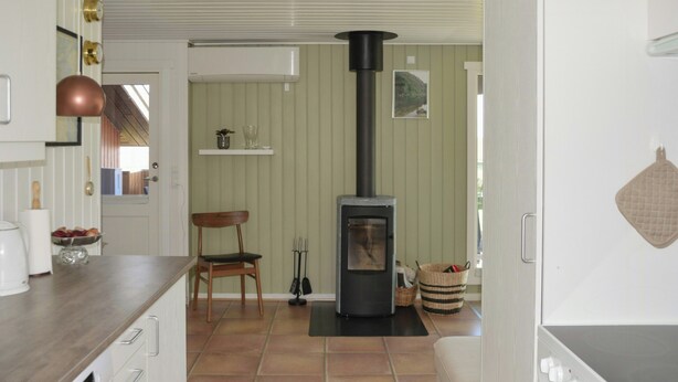 A kitchen with a wood-burning stove, a chair, a sink, and a countertop. - Summer house with sea view at Grønsund (Bogø By)