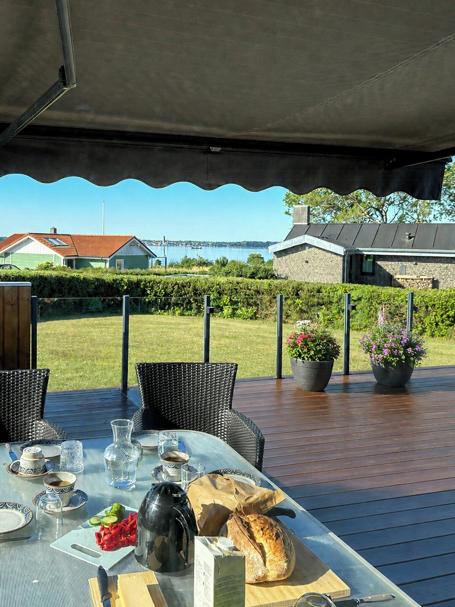 An outdoor dining area with a table set for two, overlooking a scenic landscape with a body of water and buildings in the distance.