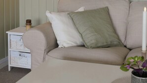Un salón con un sofá color beige, una mesita auxiliar blanca, una lámpara colgante y una obra de arte enmarcada en la pared.
