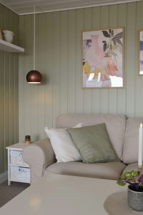 A living room with a beige sofa, a white side table, a hanging pendant light, and a framed artwork on the wall. - Summer house with sea view at Grønsund (Bogø By)