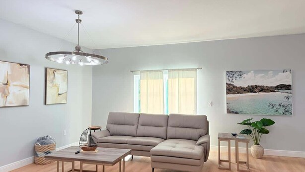 A living room with a sectional sofa, a coffee table, a pendant light, and a large window with sheer curtains. - Bright & Spacious 4/2 Home | Near Beaches & Dining (Port Charlotte)