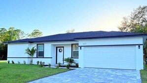 A modern single-story house with a garage, a paved driveway, and a well-maintained lawn. - Bright & Spacious 4/2 Home | Near Beaches & Dining (Port Charlotte)