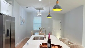 A modern kitchen with a central island, stainless steel appliances, pendant lighting, and a dining area with chairs. - Bright & Spacious 4/2 Home | Near Beaches & Dining (Port Charlotte)