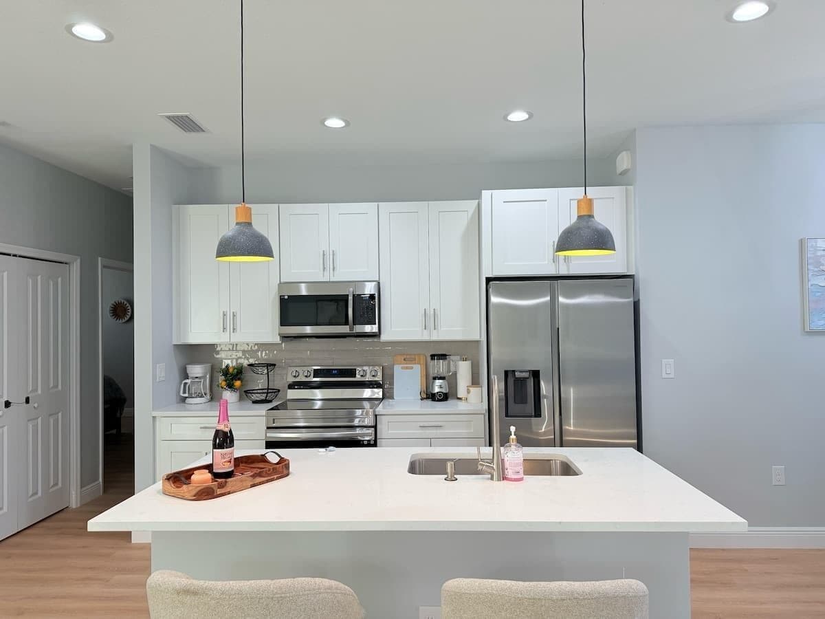 A modern kitchen with white cabinets, stainless steel appliances, and pendant lighting.