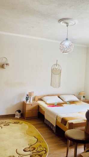 Une chambre à coucher avec un lit, des tables de chevet, une décoration murale en macramé, un luminaire au plafond et une petite lanterne blanche posée sur la table de chevet.