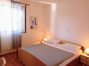 A bedroom with a bed, a nightstand, a lamp, a chair, and a window with curtains. - Apartment Amore (Rovinj)