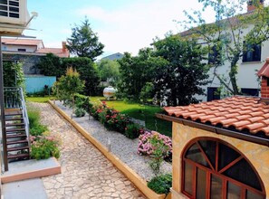 A courtyard with a stone pathway, a small garden with flowers, and a building with a tiled roof. - Apartment Amore (Rovinj)