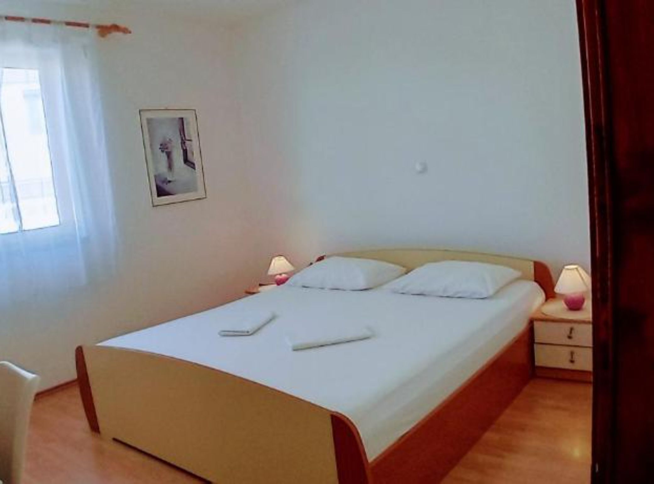 Une chambre à coucher avec un lit, des tables de chevet, une lampe, un tableau au mur et une fenêtre avec des rideaux.