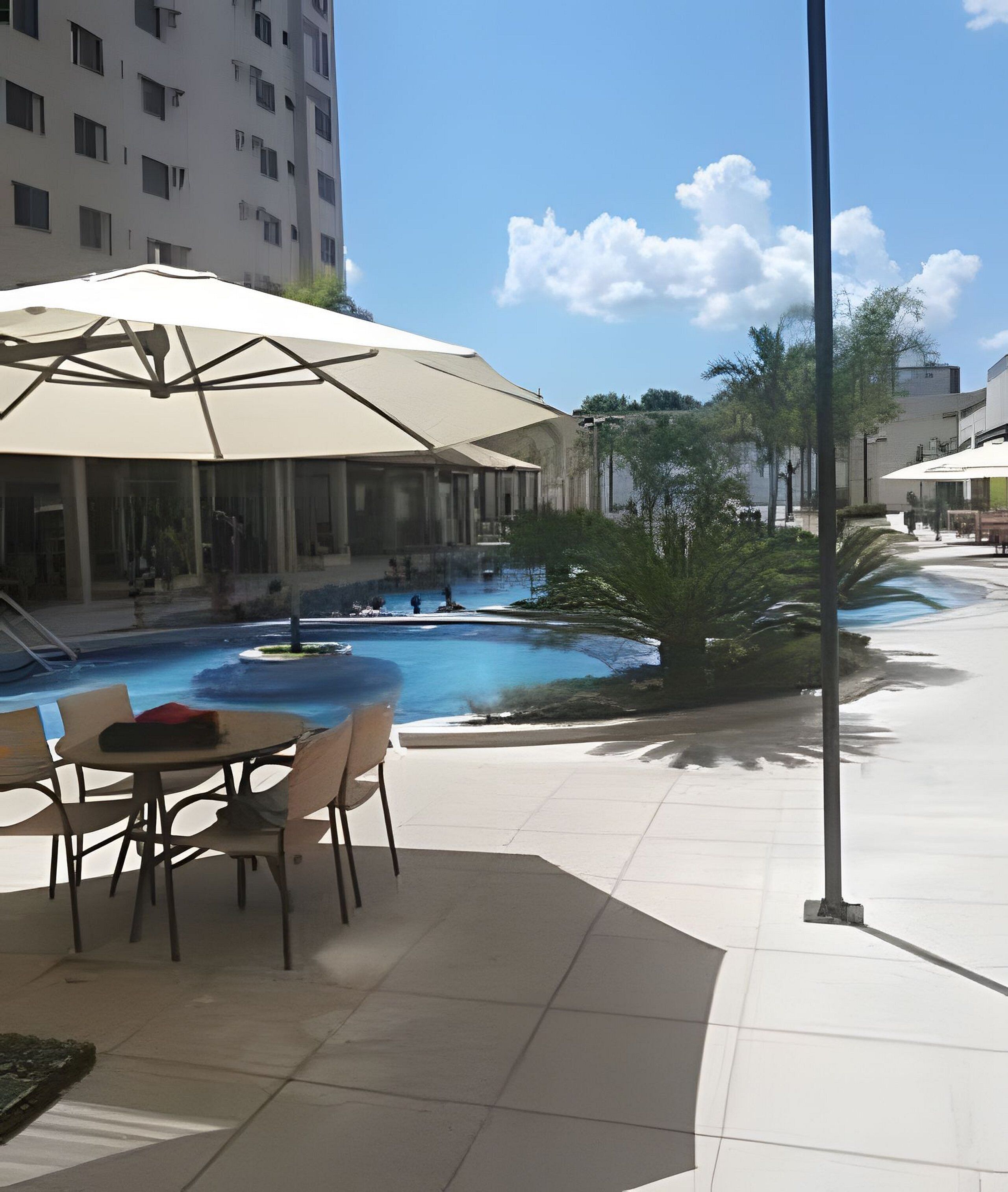 An outdoor pool area with lounge chairs and umbrellas, surrounded by buildings and trees.
