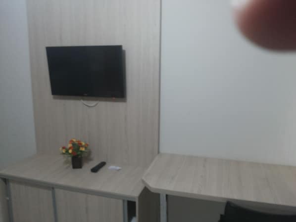 Une pièce avec un téléviseur à écran plat fixé au mur, une petite table sur laquelle se trouve un vase de fleurs et une télécommande posée sur la table.