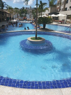 A swimming pool with a central island, surrounded by palm trees and lounge chairs. - HOTEL BOULEVARD SUITES HOTEL  (Caldas Novas)