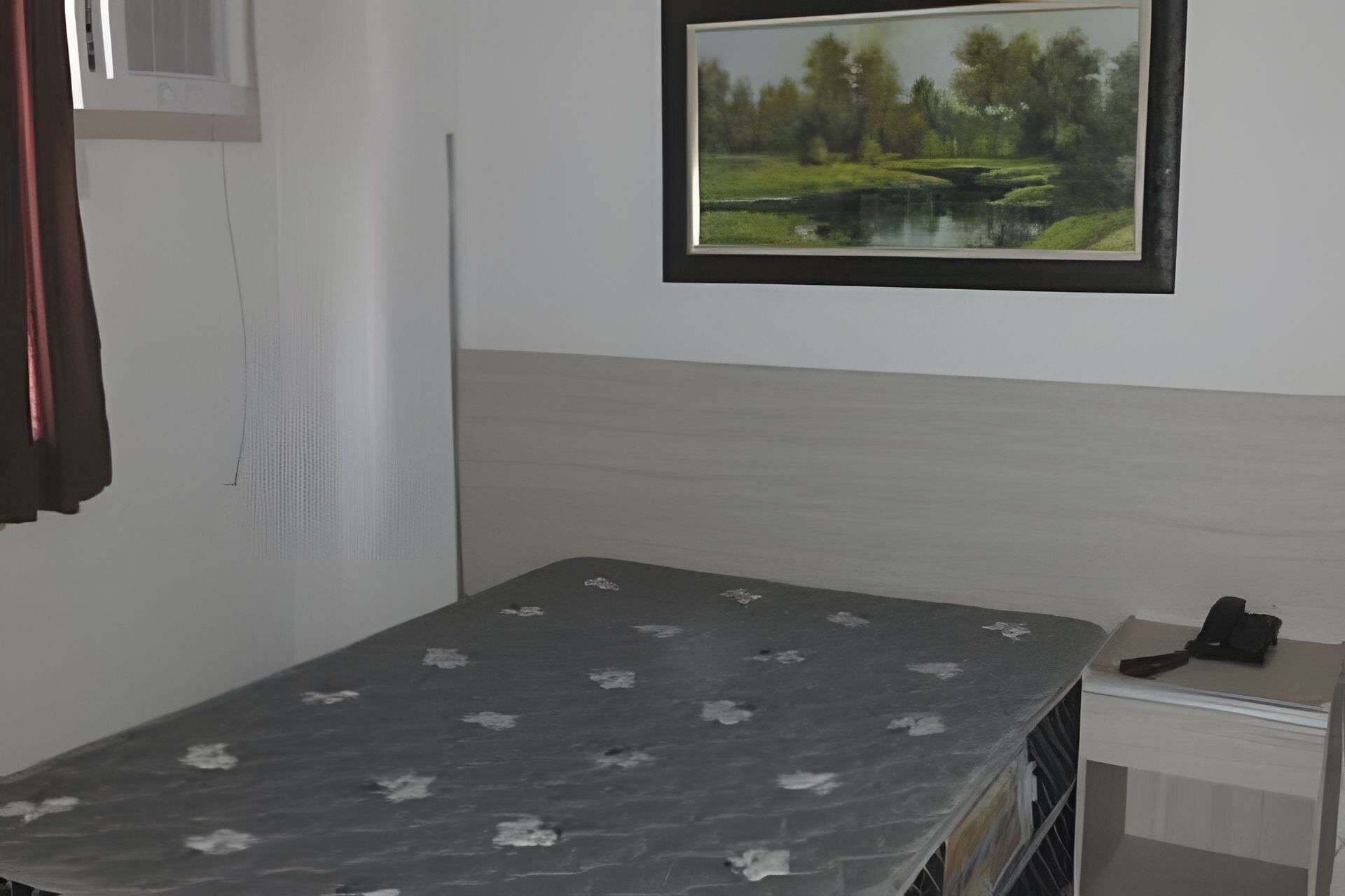 A room with a bed, a small table with a phone, and a framed landscape painting on the wall.