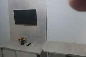 A room with a mounted television on a textured wall, a small table with a vase of flowers, and a remote control on the table.