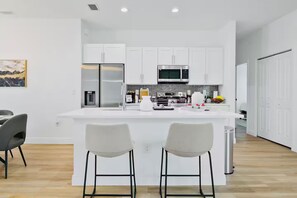 Una cocina moderna con armarios blancos, electrodomésticos de acero inoxidable y una isla central con dos taburetes de bar.