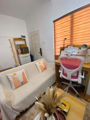 A room with a white sofa, a desk with a chair, a window with blinds, and a door. - Cozy Studio-type bungalow in welcoming Olango island, Lapu-lapu City with AC (Lapu-lapu City)