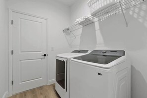 Een wasserette met twee witte wasmachines, een witte deur en een metalen droogrek.