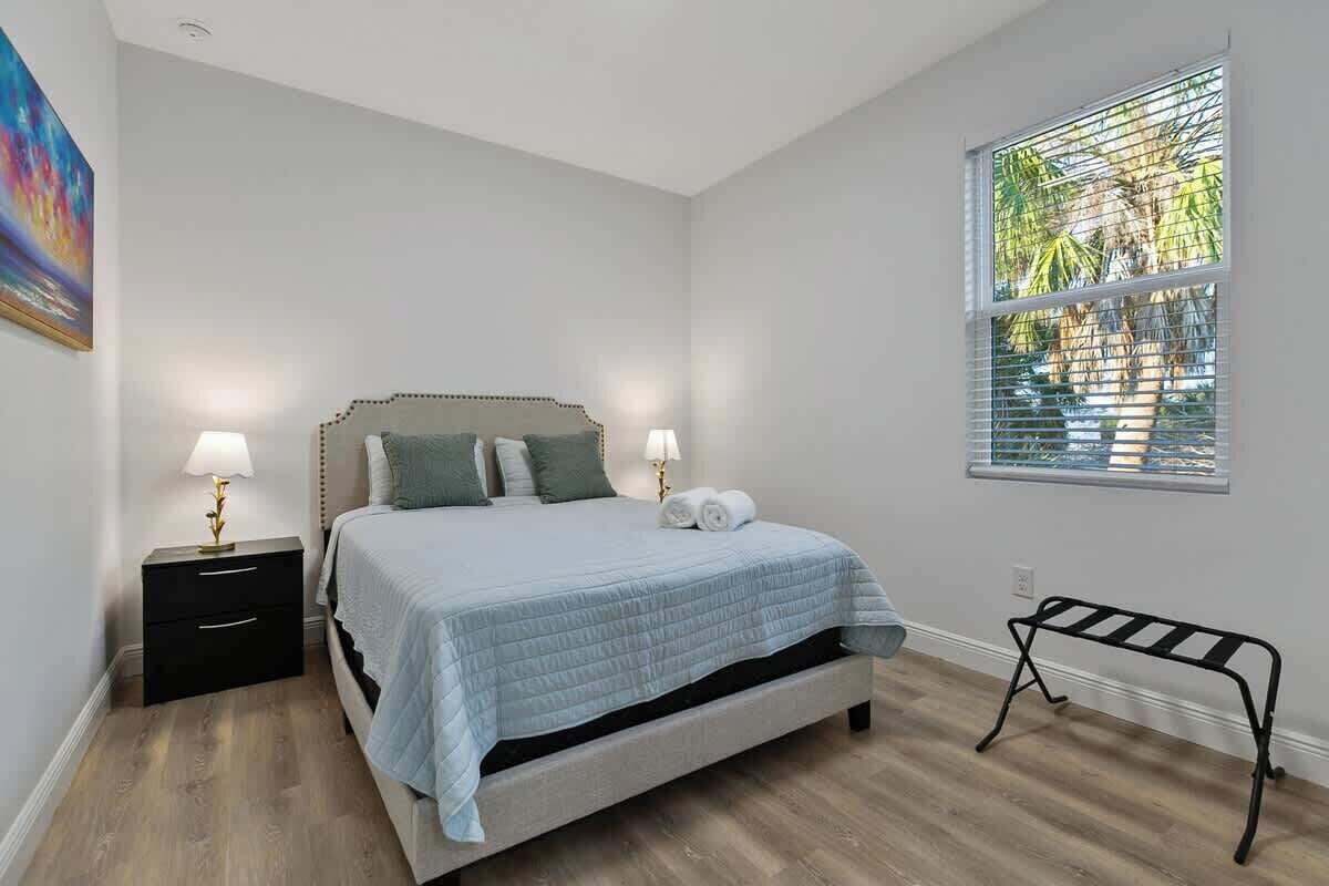 A bedroom with a bed, bedside tables, a bench, and a window with blinds.
