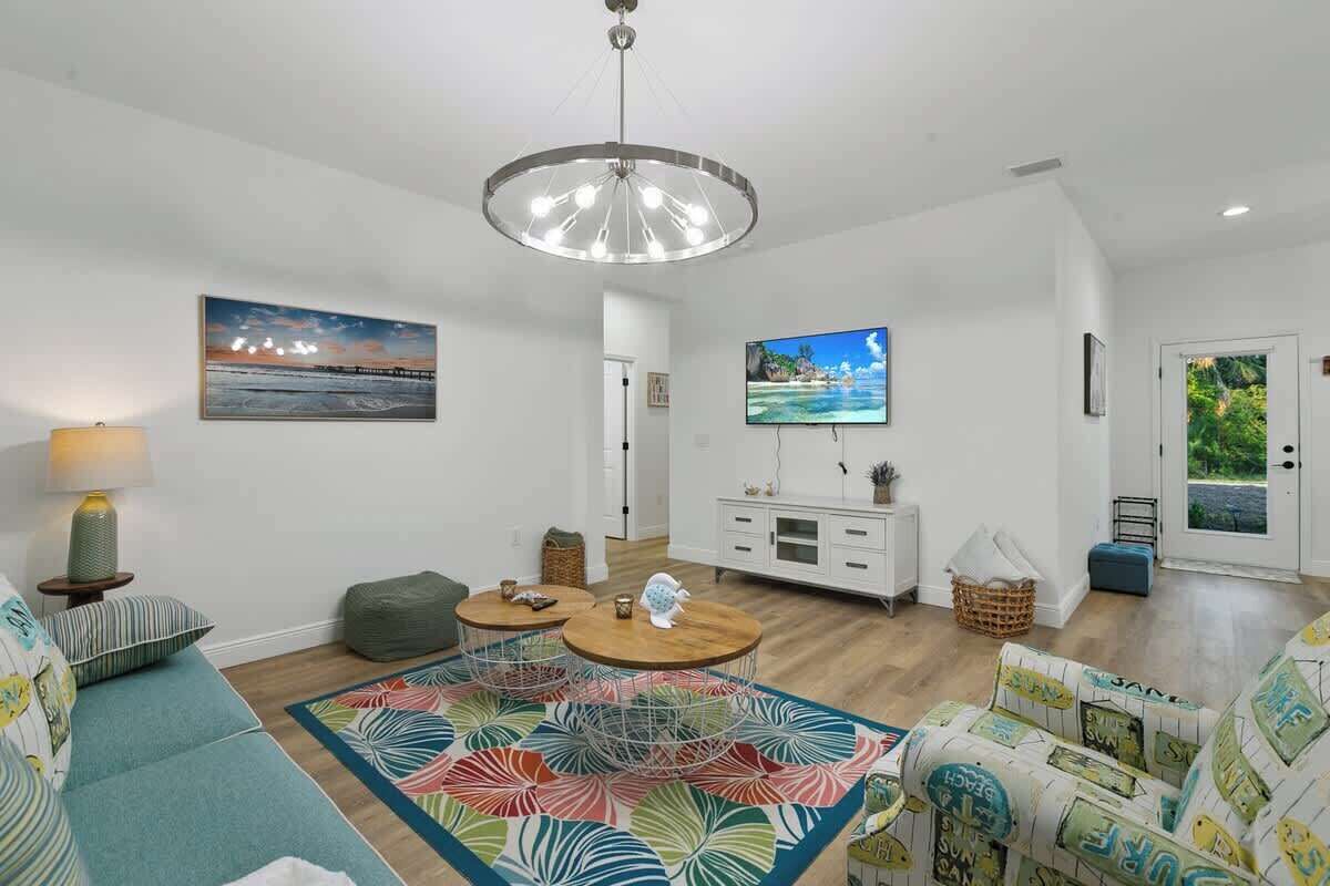 A modern living room with a large chandelier, a flat-screen TV, and a colorful rug.