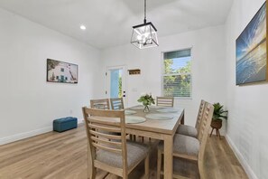 Un comedor con una mesa de madera, sillas, una lámpara colgante y una ventana con persianas.