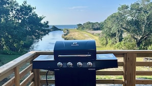 Ein Holzkohlegrill auf einer Holzterrasse mit Blick auf einen Fluss und Bäume.