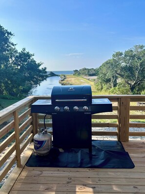 Ein Holzkohlegrill auf einer Holzterrasse mit Blick auf einen Fluss und Bäume.