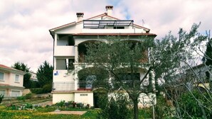 A two-story building with a balcony, surrounded by greenery and flowers. - Room Amor (Rovinj)