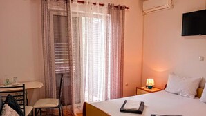 A hotel room with a bed, a desk with a chair, a nightstand with a lamp, and a window with curtains. - Room Amor (Rovinj)