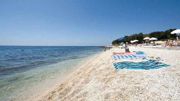 A beach with clear water, umbrellas, and people. - Room Amor (Rovinj)