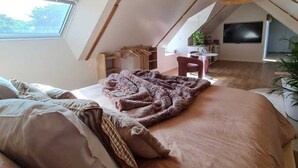 A cozy attic bedroom with a sloped ceiling, a large window, a bed with a blanket, and a hanging light fixture. - Vacation Rental 2: "La Belle Aire" at Christophe's (Le Fœil)