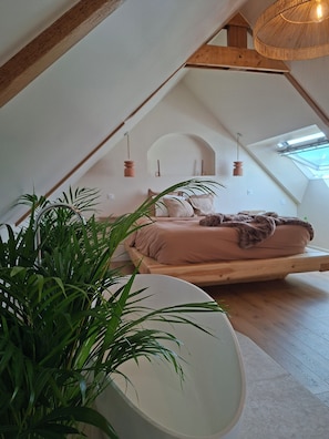 A loft bedroom with a sloped ceiling, a bed with a blanket, a hanging light fixture, and a skylight.