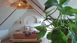 A loft bedroom with a wooden bed, a hanging light fixture, and a plant. - Vacation Rental 2: "La Belle Aire" at Christophe's (Le Fœil)