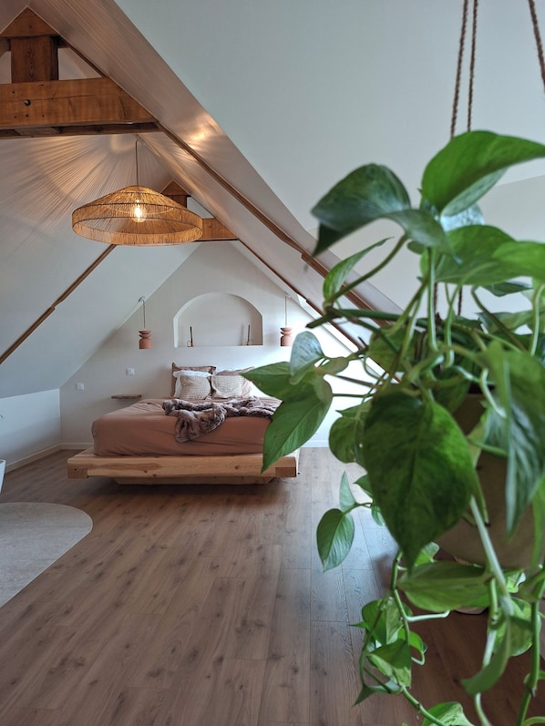 A loft bedroom with a wooden bed, a hanging light fixture, and a plant.