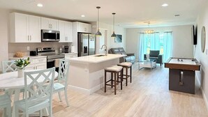 A modern kitchen with white cabinetry, stainless steel appliances, and a central island with stools. - Fresh 3BR Home, Peaceful Stay (Port Charlotte)