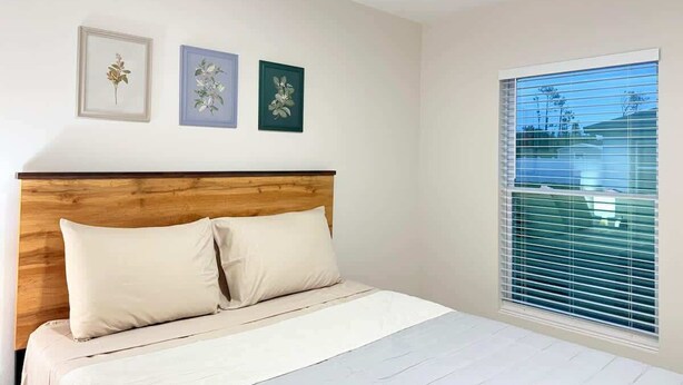 A bedroom with a wooden headboard, a bed with white bedding, and three framed floral artworks on the wall. - Fresh 3BR Home, Peaceful Stay (Port Charlotte)