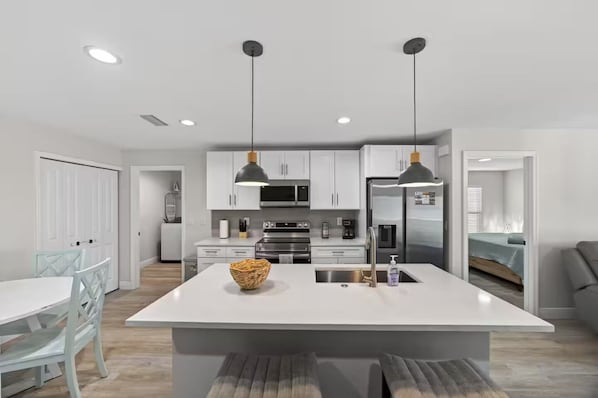 A modern kitchen with white cabinetry, stainless steel appliances, and pendant lighting.