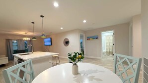 A modern kitchen with a central island, a dining area with a white table and chairs, and a television mounted on the wall. - Fresh 3BR Home, Peaceful Stay (Port Charlotte)