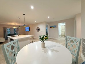 Eine moderne Küche mit einer Kochinsel, einem Essbereich mit weißem Tisch und Stühlen sowie einem an der Wand befestigten Fernseher.