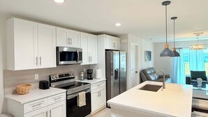 A modern kitchen with white cabinetry, stainless steel appliances, and a central island with a sink. - Fresh 3BR Home, Peaceful Stay (Port Charlotte)