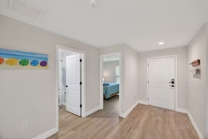 A hallway with two doors, a painting, and a bedroom visible through an open door.