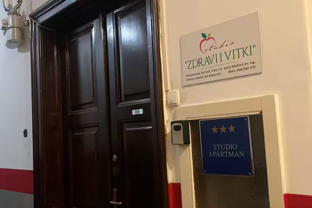 A dark wooden door with a sign above it reading 'ZDRAVI VITKI' and a blue sign below stating 'STUDIO APARTMAN'.