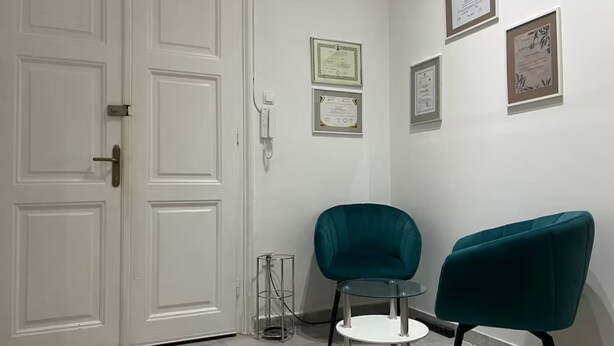 A room with a white door, a glass table, two teal chairs, and framed certificates on the wall. - Camera Munz (Pula)