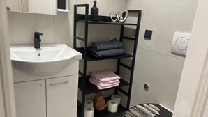 A bathroom with a white sink, a black shelf with towels, and a toilet with a black seat. - Camera Munz (Pula)