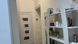 A hallway with a white door, a white bookshelf with various items, and a tiled floor. - Camera Munz (Pula)