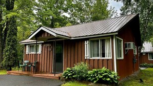 Une petite cabane en bois, de plain-pied, avec une véranda, une porte et une fenêtre.
