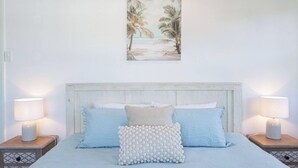 Ein Schlafzimmer mit einem Bett, zwei Nachttischen, einem Wandbild und einem Beistelltischchen mit einer Lampe.