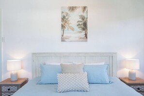 Quarto com cama, duas mesas de cabeceira, um quadro na parede e uma mesa de cabeceira com abajur.