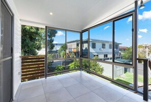 Quarto nos fundos com amplas janelas, piso de azulejos e vista para as casas vizinhas.