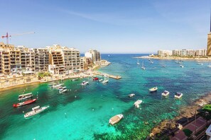 A coastal marina with multiple boats docked, a pier, and a row of multi-story buildings with balconies. - Modern 2 Bedroom Seafront Escape (Saint Julian's)